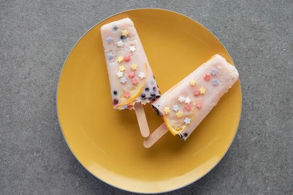Сверху вид вкусного фруктового мороженого на желтой тарелке на сером — стоковое фото