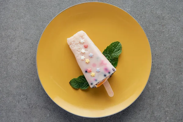 Draufsicht auf köstlich fruchtiges Eis am Stiel mit grünen Minzblättern auf gelbem Teller auf grau — Stockfoto