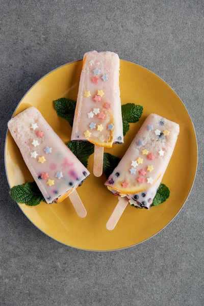 Top view of delicious fruity popsicles with green mint leaves on yellow plate on grey — Stock Photo