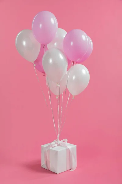 Куча шариков, привязанных на подарочной коробке на розовом фоне — стоковое фото