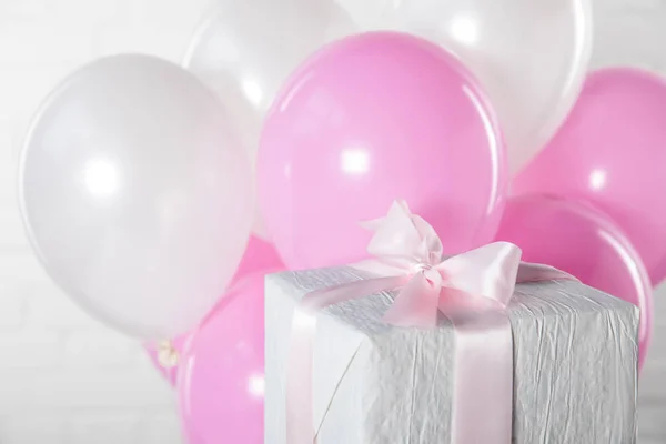 Gift box and balloons on white brick wall background — Stock Photo
