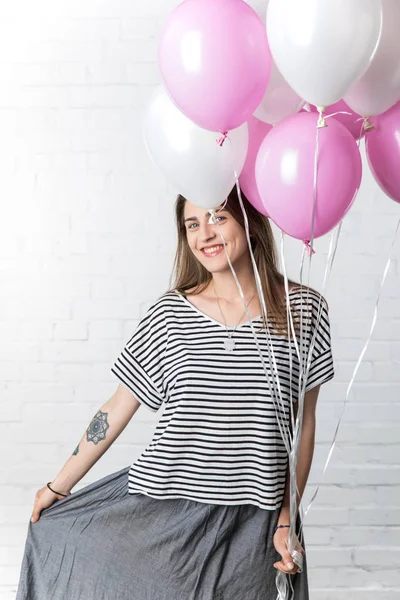 Freudige Frau posiert auf weißem Backsteinhintergrund und hält weiße und rosa Luftballons — Stockfoto