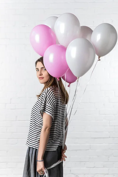 Attractive woman posing with bunch of balloons on white brick wall background — Stock Photo