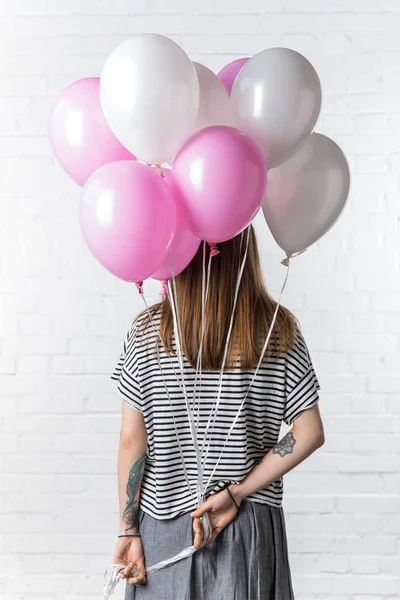 Visão traseira da mulher com balões rosa e branco no fundo da parede de tijolo branco — Fotografia de Stock