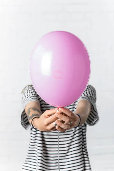 Chica sosteniendo globo rosa en frente de su cara sobre fondo de pared de ladrillo blanco - foto de stock