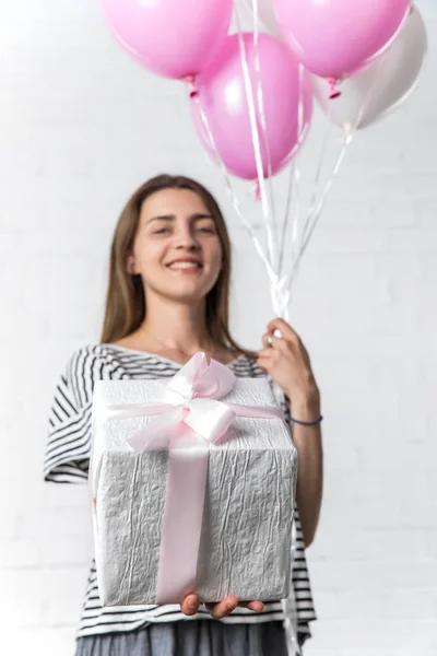 Presente y globos en las manos de la joven sobre fondo de pared de ladrillo blanco - foto de stock