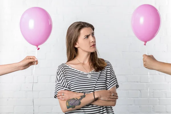 Thoughtful young woman looking at hand holding balloon on white brick wall background — Stock Photo