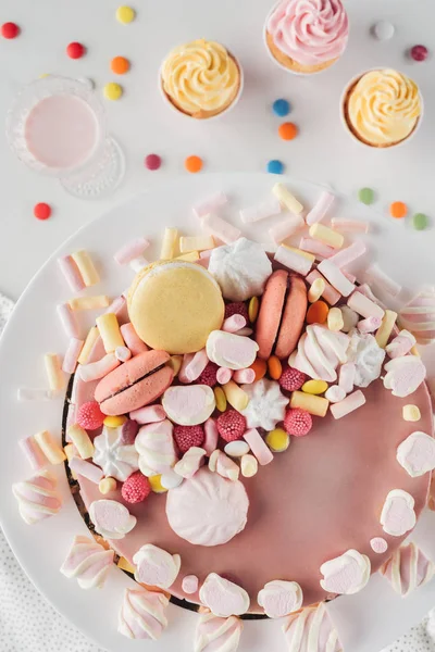 Top view of sweet birthday cake with marshmallows on marble table with milkshake and cupcakes — Stock Photo