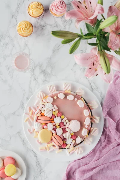 Top view of sweet birthday cake with marshmallows and pink lily flowers on marble table — Stock Photo