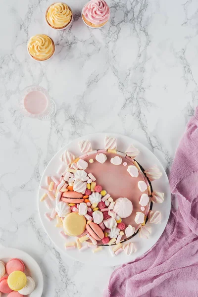 Flat lay with pink birthday cake with marshmallows, cupcakes and milkshake on marble table — Stock Photo