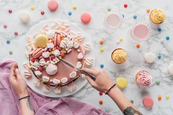 Corte vista de mulher tatuada corte rosa bolo de marshmallow com faca na mesa — Fotografia de Stock