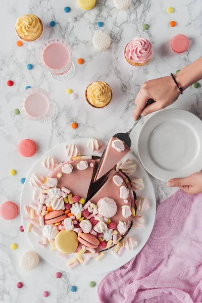 Vista recortada de la mujer poniendo pedazo de pastel de cumpleaños rosa con malvaviscos en el plato - foto de stock