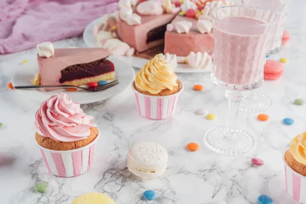 Primer plano de pastel rosa, malvaviscos, caramelos, magdalenas dulces y batido en la mesa de mármol - foto de stock