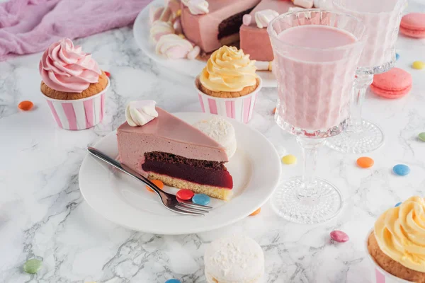 Morceau de gâteau d'anniversaire, bonbons, cupcakes sucrés et milkshake sur table en marbre — Photo de stock
