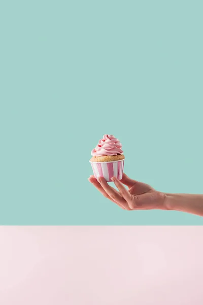 Vista recortada de la mujer sosteniendo cupcake con crema de mantequilla rosa - foto de stock