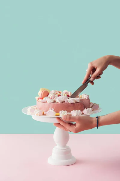 Cropped view of woman cutting pink marshmallow cake with knife on cake stand — Stock Photo