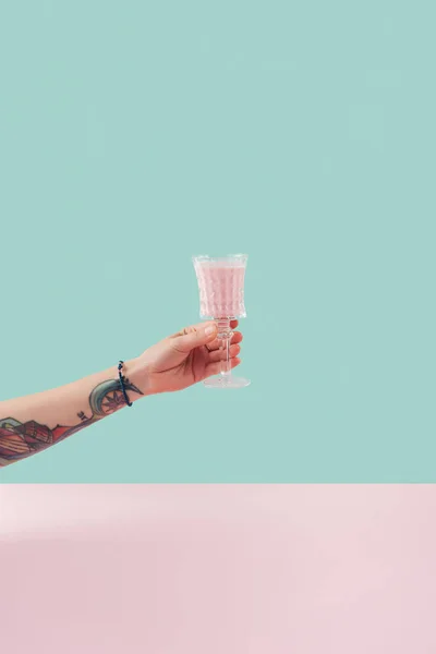 Vista recortada de la mano tatuada femenina con vaso de batido sobre fondo pastel - foto de stock