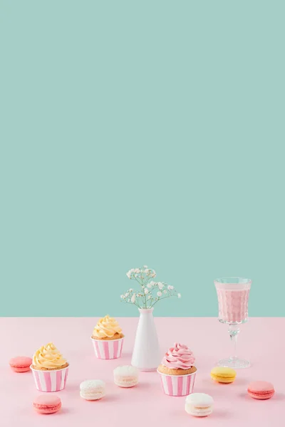 Cupcakes, macarons, milkshake and flowers in vase on pastel background with copy space — Stock Photo