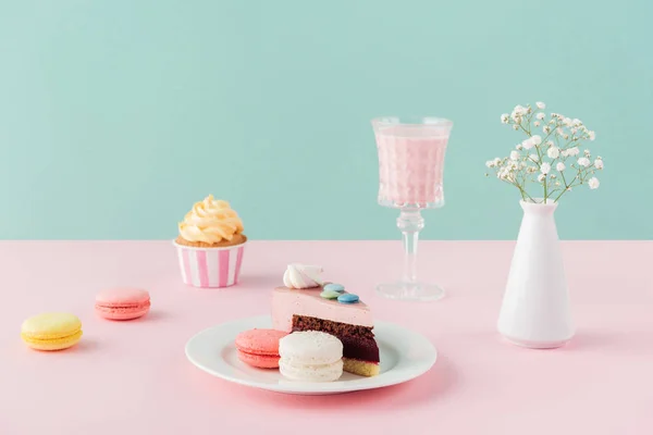 Macarons, Cupcake, Kuchenstück und Milchshake auf Pastell-Hintergrund — Stockfoto