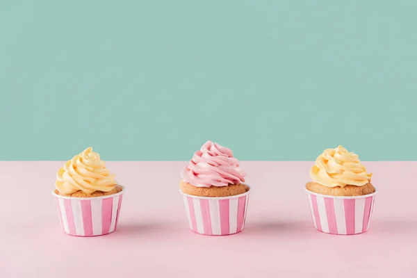 Três cupcakes com creme de manteiga em linha no fundo pastel — Fotografia de Stock