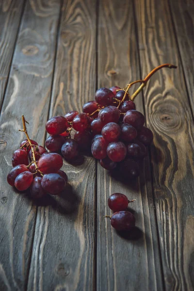 Close-up shot of branches of red grapes on rustic wooden table — Stock Photo