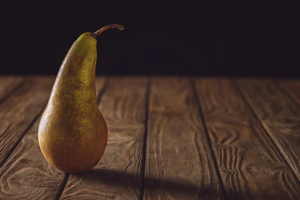 Close-up shot of ripe pear on rustic wooden table on black — Stock Photo