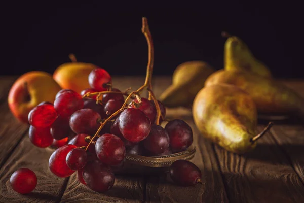 Close-up shot of ripe pears and grapes on rustic wooden table on black — Stock Photo