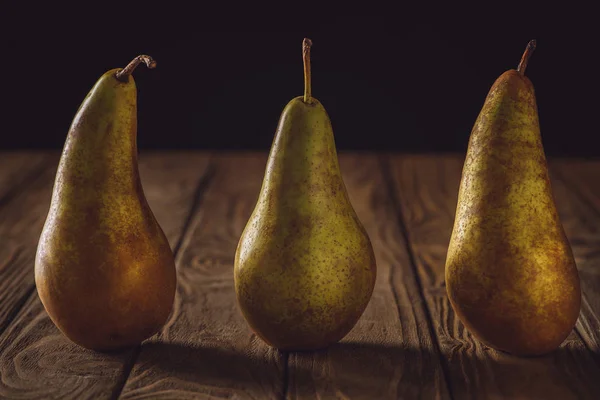 Close-up shot of ripe pears in row on rustic wooden table on black — Stock Photo