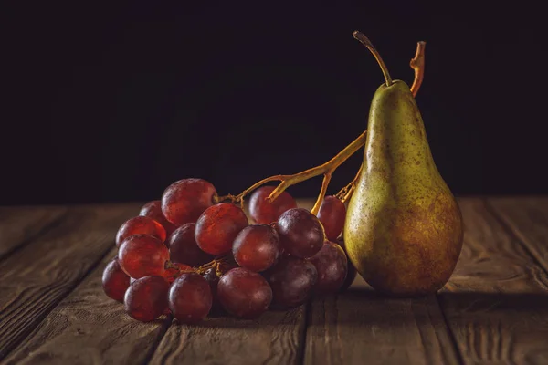 Close-up de pêra madura e uvas na mesa de madeira rústica em preto — Fotografia de Stock