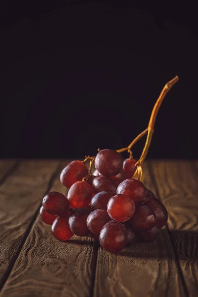 Primer plano de uvas rojas maduras sobre mesa de madera rústica sobre negro - foto de stock