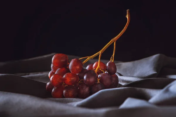 Primer plano de uvas rojas maduras sobre una cortina gris sobre negro - foto de stock