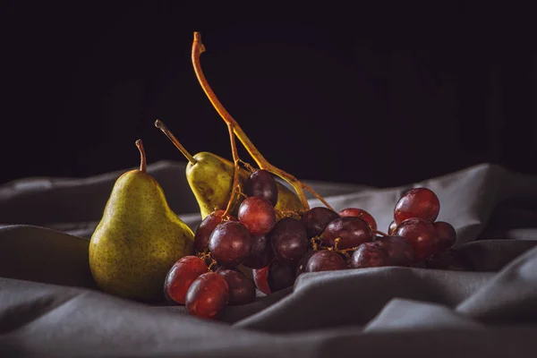 Close-up de pêra madura e uvas vermelhas em cortinas cinza em preto — Fotografia de Stock