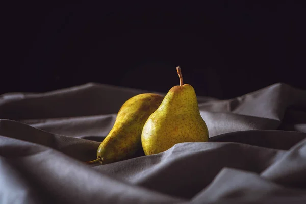 Gros plan de poires jaunes mûres sur des draperies grises sur du noir — Photo de stock