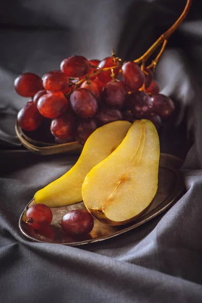 Close-up de pêra fatiada e uvas vermelhas em cortinas cinzentas — Fotografia de Stock