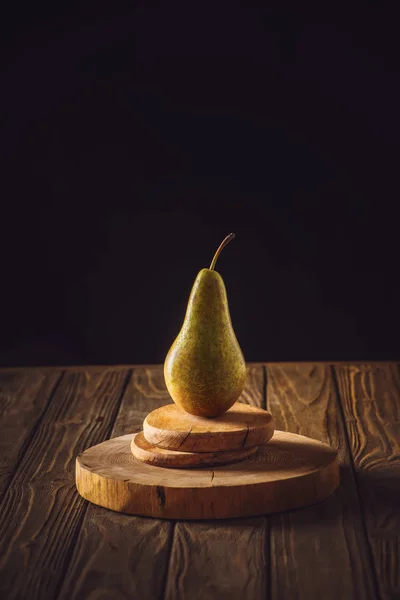 Close-up shot of ripe pear on stacked boards and on rustic wooden table on black — Stock Photo