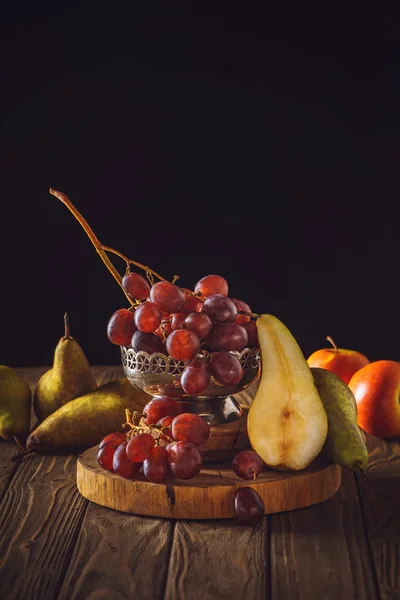 Close-up shot of ripe grapes with pears on rustic wooden table on black — Stock Photo