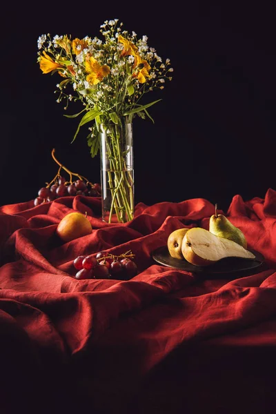 Nature morte avec différents fruits et fleurs en vase sur draperie rouge sur noir — Photo de stock