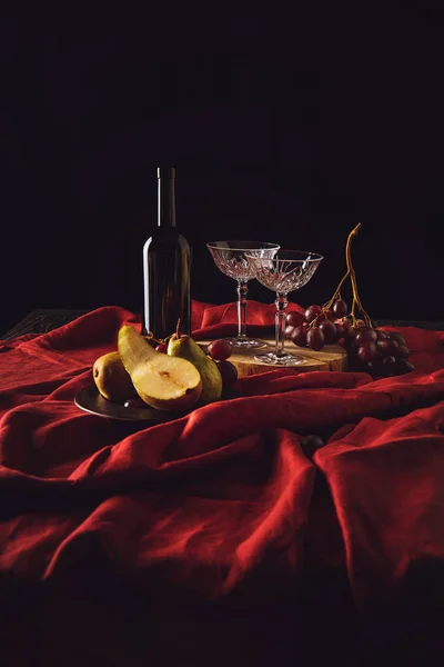 Натюрморт с грушами, виноградом и вином на красной драпировке на черном — стоковое фото