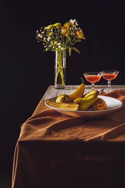 Assiette de poires avec verres de vin et bouquet sur table sur fond noir — Photo de stock