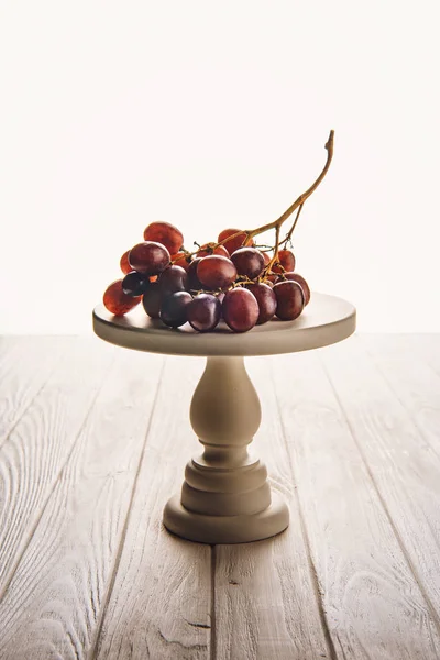 Close-up shot of branch of grapes on stand on wooden table — Stock Photo