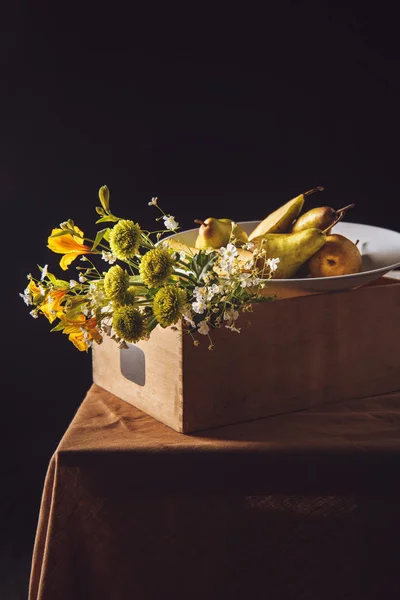 Close-up shot of bouquet of field flowers with pears in box on black — Stock Photo