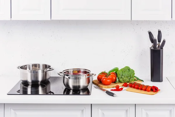 Стиглі овочі на кухонній лічильнику, каструлі на електричній плиті на легкій кухні — стокове фото