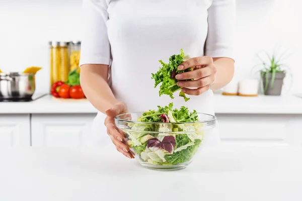 Обрізане зображення жінки, що тримає миску з листям салату на світлій кухні — стокове фото