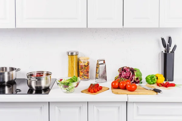 Légumes mûrs sur planches à découper, casseroles sur cuisinière électrique dans la cuisine légère — Photo de stock