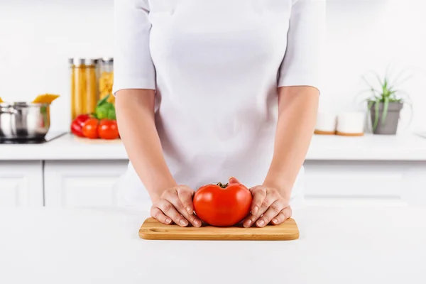 Cropped image of woman holding ripe tomato on cutting board in light kitchen — Stock Photo