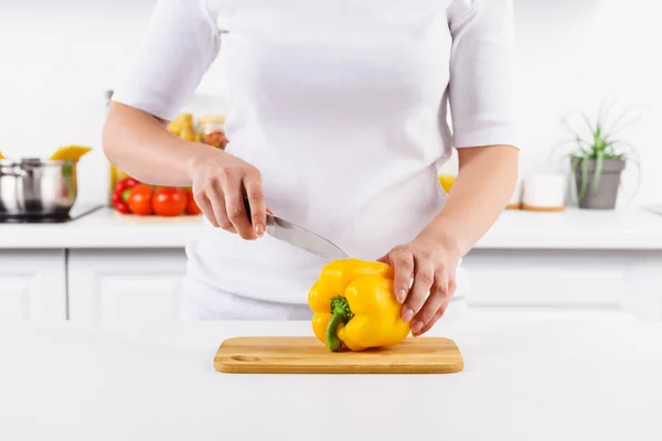 Cropped image of woman cutting yellow bell pepper in light kitchen — Stock Photo