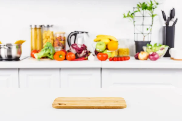 Empty cutting board on table with ripe vegetables on background in light kitchen — Stock Photo