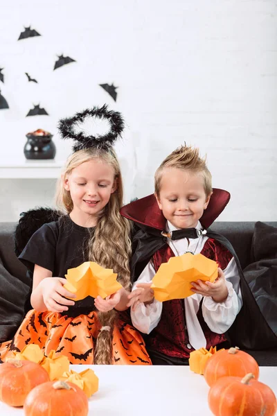 Портрет маленьких братів і сестер в костюмах Хеллоуїна, що сидять на дивані за столом з гарбузами вдома — стокове фото