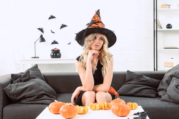 Portrait de femme coûteuse en costume de sorcière assis à la table basse avec des citrouilles, concept de vacances d'Halloween — Photo de stock