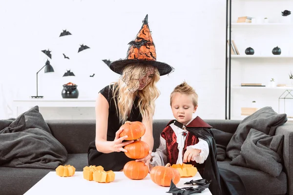 Retrato de la madre y el hijo en trajes de Halloween sentado en la mesa de café con calabazas en casa - foto de stock